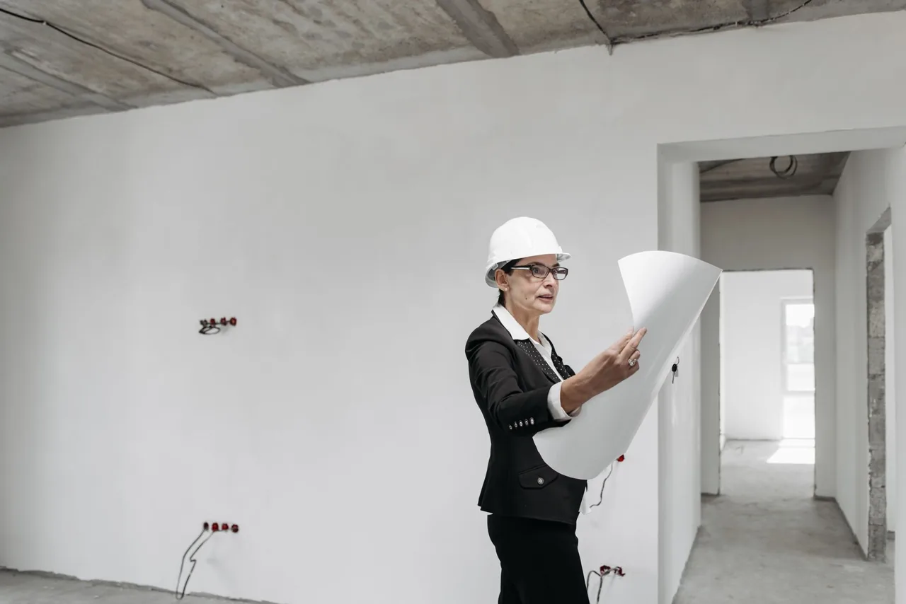 Architektin mit weißem Schutzhelm prüft Baupläne auf einer Baustelle im Rohbau