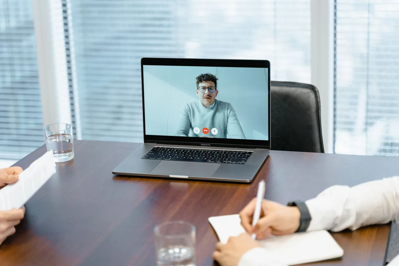 Person nimmt an einer Video-Beratung per Laptop teil und macht Notizen – digitale Beratung beim Jobcenter
